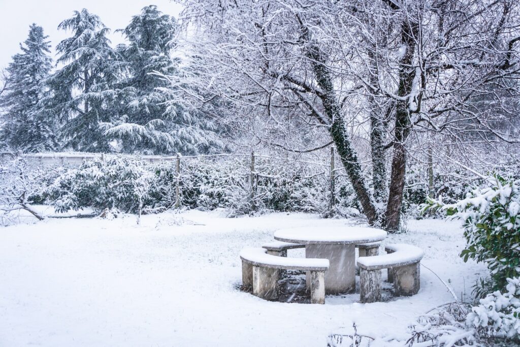 a snow covered park bench sitting in the middle of a forest