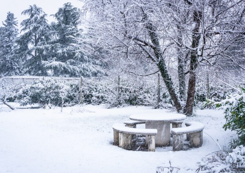 a snow covered park bench sitting in the middle of a forest